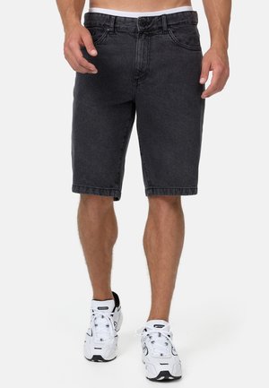 Des shorts en denim noir avec une coupe standard, cinq poches et une taille avec des passants de ceinture. Associés à des chaussures de sport blanches.