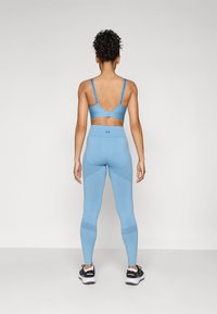 Világoskék sportmelltartó és hozzáillő leggings, ruganyos anyagból, bordás részletekkel és márkajelzéssel a pántokon. Fekete sportcipők.