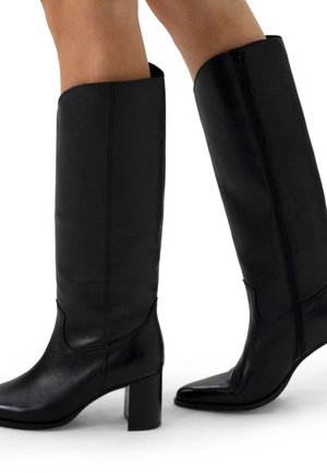 Bottes en cuir noir montantes avec une texture lisse, talon carré bloc et fermeture éclair sur le côté. Bout pointu et design supérieur contourné.