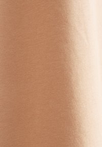 Nahaufnahme eines glatten, hellbraunen Stoffes mit feiner Strickstruktur und weichen Schatten, die die Oberfläche des Materials hervorheben.