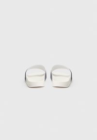 Λευκά σανδάλια τύπου slide με λείο, υφή υποδήματος και ανοιχτό δάχτυλο. Διαθέτουν αντίθετες ρίγες σε σκούρο μπλε στα πλευρά.