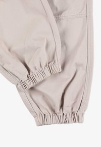 Jasne beżowe spodnie z tkaniny z elastycznymi mankietami, charakteryzujące się gładką fakturą i poziomymi detalami szwów.