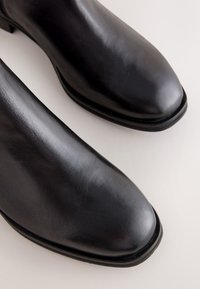 Zwarte leren enkellaarsjes met een gladde textuur, puntige neus en dunne rubberen zool. Heeft minimale stiksels en een slank ontwerp.