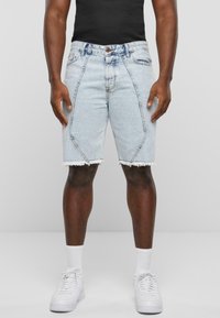 Denim šorti ar gaiši zilā mazgājumā, saplēstiem galiem un slīpiem šuvēm. Kombinēti ar melnu topu un baltām sporta apaviem.