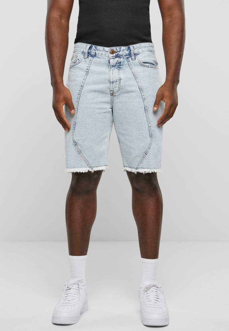 Denim šorti ar gaiši zilā mazgājumā, saplēstiem galiem un slīpiem šuvēm. Kombinēti ar melnu topu un baltām sporta apaviem.