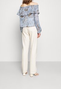 Blusa azul claro con hombros al descubierto y detalle de volantes, patrón floral en marrón y crema, combinada con pantalones de pierna ancha en crema y sandalias de tacón cuadrado.