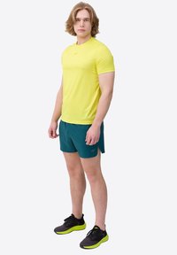 Geel sportshirt met korte mouwen, turquoise shorts en zwarte sneakers met neonzolen; gladde textuur en aansluitend ontwerp.