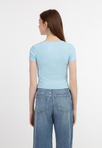 Lyseblå ribbet top med korte ærmer og scoop-hals, parret med højtaljede, falmede blå denimjeans med to baglommer.