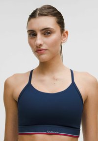 Granatowy stanik sportowy z cienkimi ramiączkami, gładkim materiałem i kontrastowym czerwono-białym pasem na dole z logo lululemon.