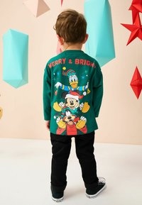 Roheline pika varrukaga särk, millel on joonistatud koomiksitegelased Miki Hiir, Donald Duck ja Goofy, koos punase tekstiga "MERRY & BRIGHT". mustad püksid.