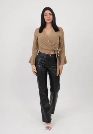 Top avvolgente khaki con maniche lunghe a campana e dettagli con bottoni, abbinato a pantaloni neri in ecopelle a vita alta e décolleté bianchi con lacci.