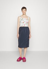 Top cropped branco bordado com flores e alças finas, combinado com uma saia azul escura com cordão e sapatos plataforma rosa-choque.