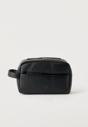 Trousse de toilette en cuir noir avec fermeture éclair, poche avant et poignée latérale sur fond clair uni.