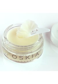 Barattolo trasparente di crema con una sfumatura gialla pallida, coronato da una cucchiaiata di panna bianca e soffice. Presenta il nome del marchio "OSKIA LONDON" in caratteri eleganti.