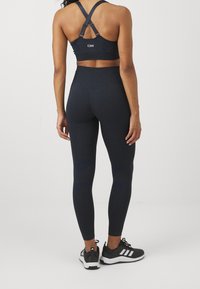 Marinblå sportbehå med korsryggsremmar, kombinerad med högmidjade marinblå leggings som har texturerade detaljer och en slät yta.