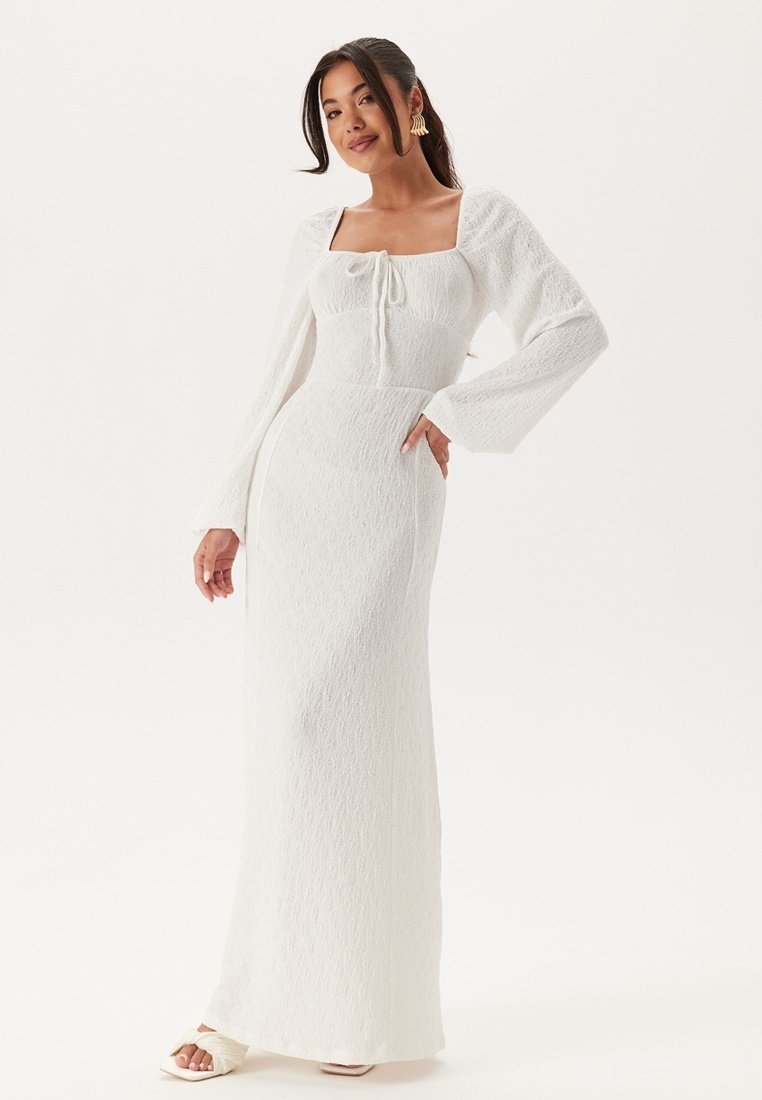 Witte langemouwjurk met een vierkante halslijn, trekkoorddetail, gestructureerde stof en een aansluitende silhouet, die tot de vloer vloeit.