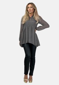 Czarna bluzka w kwiatowy wzór z długimi rękawami i marszczonym pasem, zestawiona z dopasowanymi czarnymi spodniami i złotymi butami na platformie.