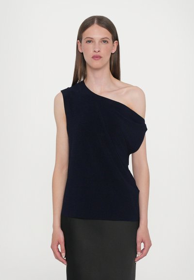 Top blu navy a spalla unica realizzato in tessuto morbido, con dettagli drappeggiati e una vestibilità ampia, abbinato a una gonna nera.
