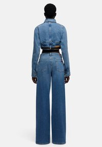 Strój z denimu składający się z krótkiej kurtki i szerokich spodni jeansowych, oba w średnim odcieniu niebieskiego, o gładkiej fakturze i klasycznym, pięciokieszeniowym kroju.