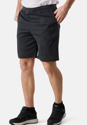 Schwarze Sportshorts mit einem elastischen Bund, Seitentaschen, einer glatten Textur und einem leicht melierten Muster. Kombiniert mit schwarzen Sneakers.