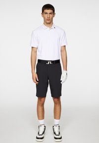 Vit pikétröja för män, svarta shorts, svart bälte med silverspänne, vita handskar, svartvita sneakers. Smooth tyg och skräddarsydd passform.