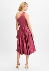 Robe en satin à une épaule de couleur rose profond, présentant un corsage ajusté, une jupe plissée et une longueur moyenne, associée à des talons neutres à lanières.