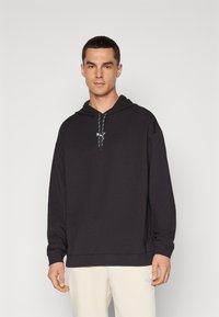 Sudadera negra con bolsillo tipo canguro, capucha con cordón y puños acanalados. Presenta un logo sutil en el pecho y un corte relajado.