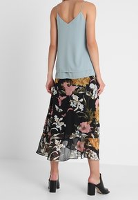 Camisole bleu clair à fines bretelles associée à une jupe noire à motifs floraux colorés avec un ourlet à volants superposés. Chaussures noires à talons blocs.