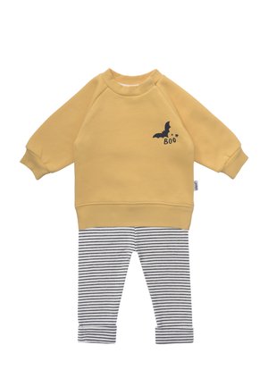 Gelber Pullover mit einer Fledermausgrafik und dem Text "Boo", kombiniert mit schwarz-weiß gestreiften Leggings. Weicher Stoff, lockere Passform, gerippte Bündchen.