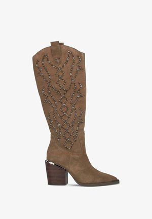 Bota de ante marrón hasta la rodilla con punta afilada, adornada con tachuelas de metal en un patrón geométrico. Cuenta con un tacón de madera grueso.