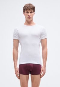 Witte katoenen T-shirt met korte mouwen, nauwsluitend ontwerp. Draagt bijpassende wijnrode boxershorts. Eenvoudige, gladde textuur en klassieke stijl.