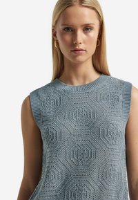 Ärm-lös ljusblå stickad tröja med geometriska mönster, ribbad halsringning och ärmhål, samt en strukturerad, öppen design.