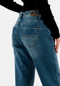 Jeans in denim azzurro chiaro con una vestibilità rilassata, dotati di una cintura intrecciata, doppie tasche posteriori e cuciture decorative sui bordi delle tasche.