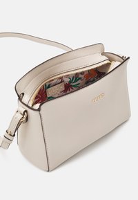 Bolso de mano de imitación cuero beige con un diseño estructurado, cremallera dorada y forro estampado de flores. Cuenta con una correa de hombro desmontable.