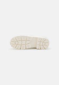 Semelle d'une basket, présentant un caoutchouc blanc épais et texturé avec des motifs de semelle profonds pour une meilleure adhérence et durabilité.
