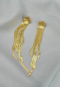 Goldfarbene Haarnadeln mit länglichem, wellenförmigem Design. Glatte Textur, glänzende Oberfläche, mit flachen oberen Abschnitten. Vor einem silbernen Hintergrund platziert.