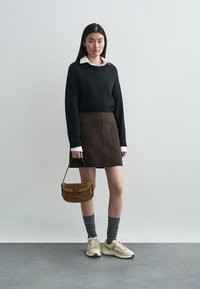 Sort striktrøje, brun ruskindnederdel med frontlommer, grå knæstrømper og cremefarvede sneakers. Brun håndtaske med nitter.