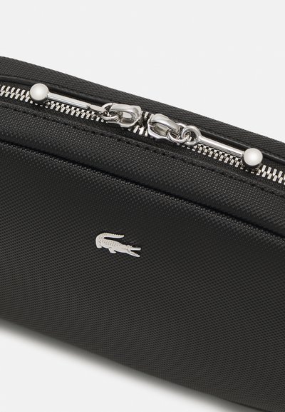 Pochette de voyage noire texturée avec quincaillerie argentée et fermeture à zip, présentant un petit logo embossé à l'avant.