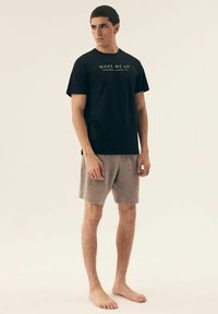 Czarny bawełniany t-shirt z napisem "OBUDŹ MNIE", zestawiony z jasnoszarymi szortami, prezentujący prosty design i luźny krój.