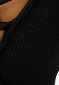 Close-up van donker geribbeld fabric met een uitgesneden detail waaronder een bruine huid zichtbaar is.