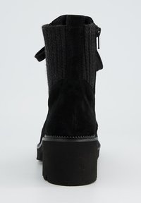 Bottine noire avec une tige en tissu texturé, en suède, une semelle en caoutchouc plate et une fermeture éclair sur le côté pour un enfilage facile.