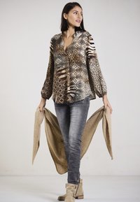 Printed blouse with animal patterns in brown and beige tones, paired with gray skinny jeans and a textured beige wrap.