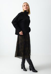Schwarzer Strickpullover mit Rollkragen, kombiniert mit einem gefältelten Rock mit dunklem Muster und kniehohen schwarzen Stiefeln. Strukturierte Materialien schaffen einen visuellen Kontrast.