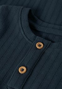 Tessuto in maglia a coste di un blu navy scuro, con una finitura testurizzata, caratterizzato da due bottoni in legno sul collo per la chiusura.