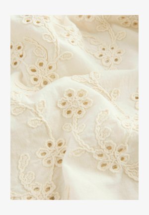 Išsiuvinėta medžiaga, kuri turi sudėtingus gėlių raštus švelnia kremine spalva siūlais ant minkšto, kreminio fono, parodantį subtilias tekstūras ir raštus.