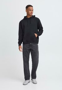 Svart bomullssweater med kengurulomme, parret med mørkegrå jeans og grå sneakers. Har en hette med snor og ribbestrikkede mansjetter.