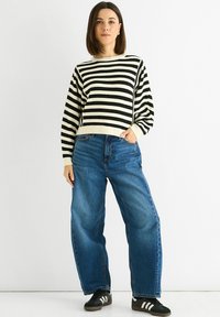 Black and white striped knit sweater with a crew neck, paired with loose blue denim jeans and black sneakers with white stripes.