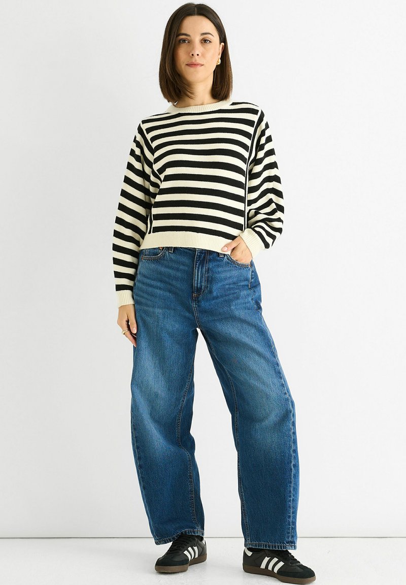 Black and white striped knit sweater with a crew neck, paired with loose blue denim jeans and black sneakers with white stripes.