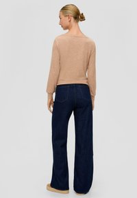 Beige langemouwtop gecombineerd met donkerblauwe wijde jeans. Eenvoudig ontwerp, zachte textuur, zichtbare stiksels op de jeans en getextureerde zolen op de schoenen.