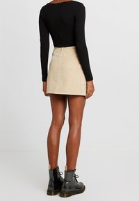 Gonna mini in corduroy beige con taglio dritto, tasche posteriori e superficie texturizzata, abbinata a stivaletti neri con lacci alla caviglia.